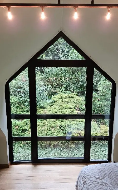 Grande fenêtre fixe en pointe de pignon, profilés noirs, du sol au plafond